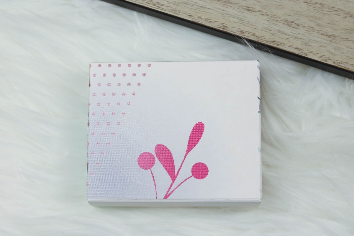 Einzelner Karton aus dem Amorelie Kalender mit rosa Zweig auf weißem Fell.