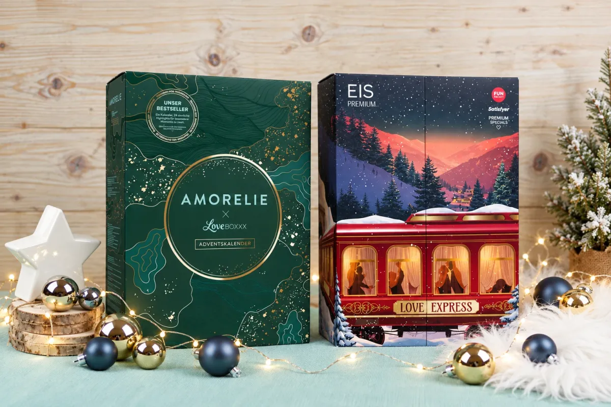 Der grüne Amorelie Adventskalender 2026 und der rote EIS Premium Adventskalender nebeneinander zwischen Christbaumkugeln und Lichterkette, die beiden Kalender im Vergleich Amorelie oder EIS.